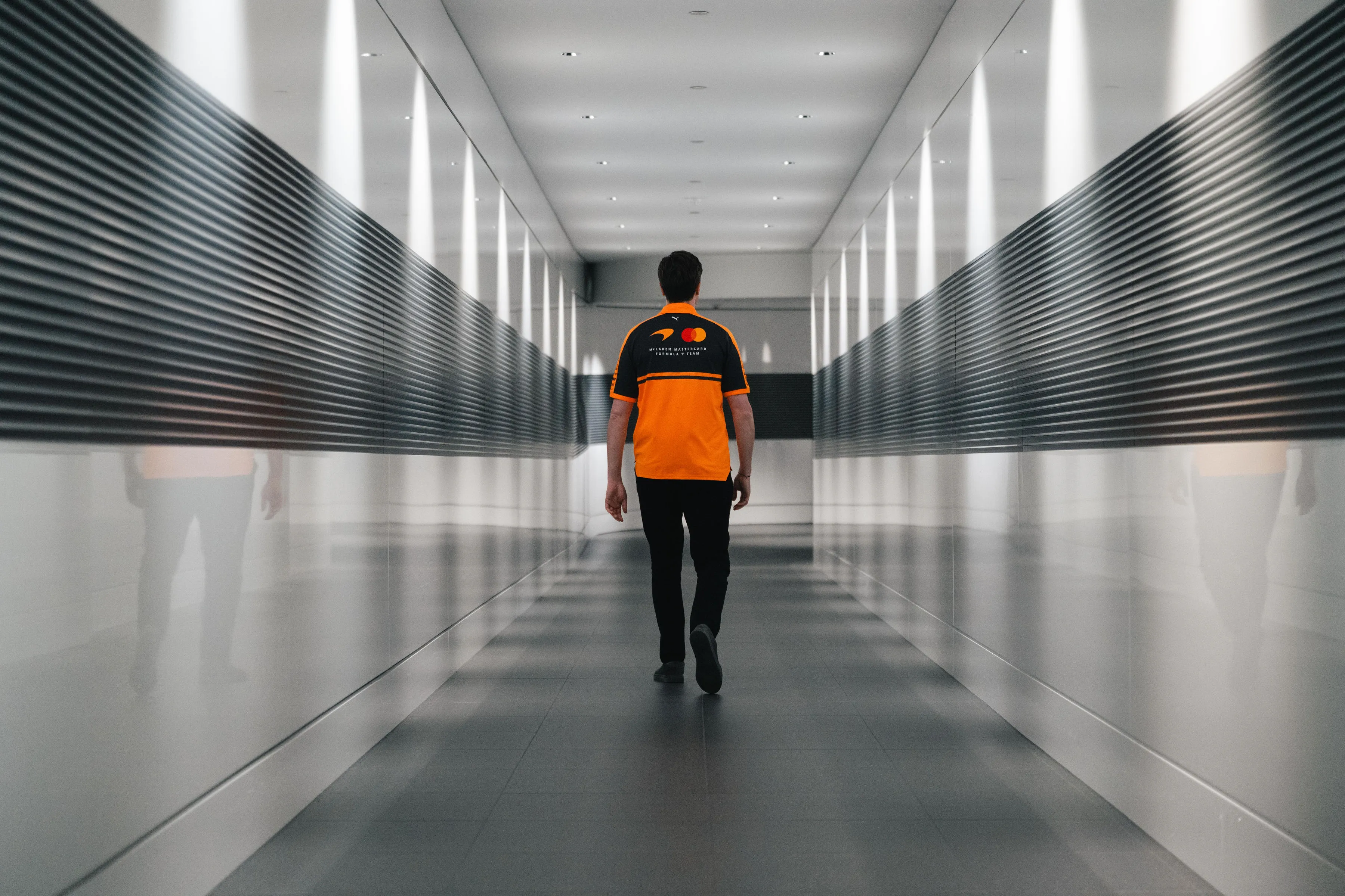Team member walking away from camera down a mirrored corridor at the McLaren Technology Centre