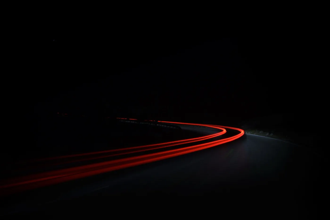 Red tail-light trails curving through a dark mountain road